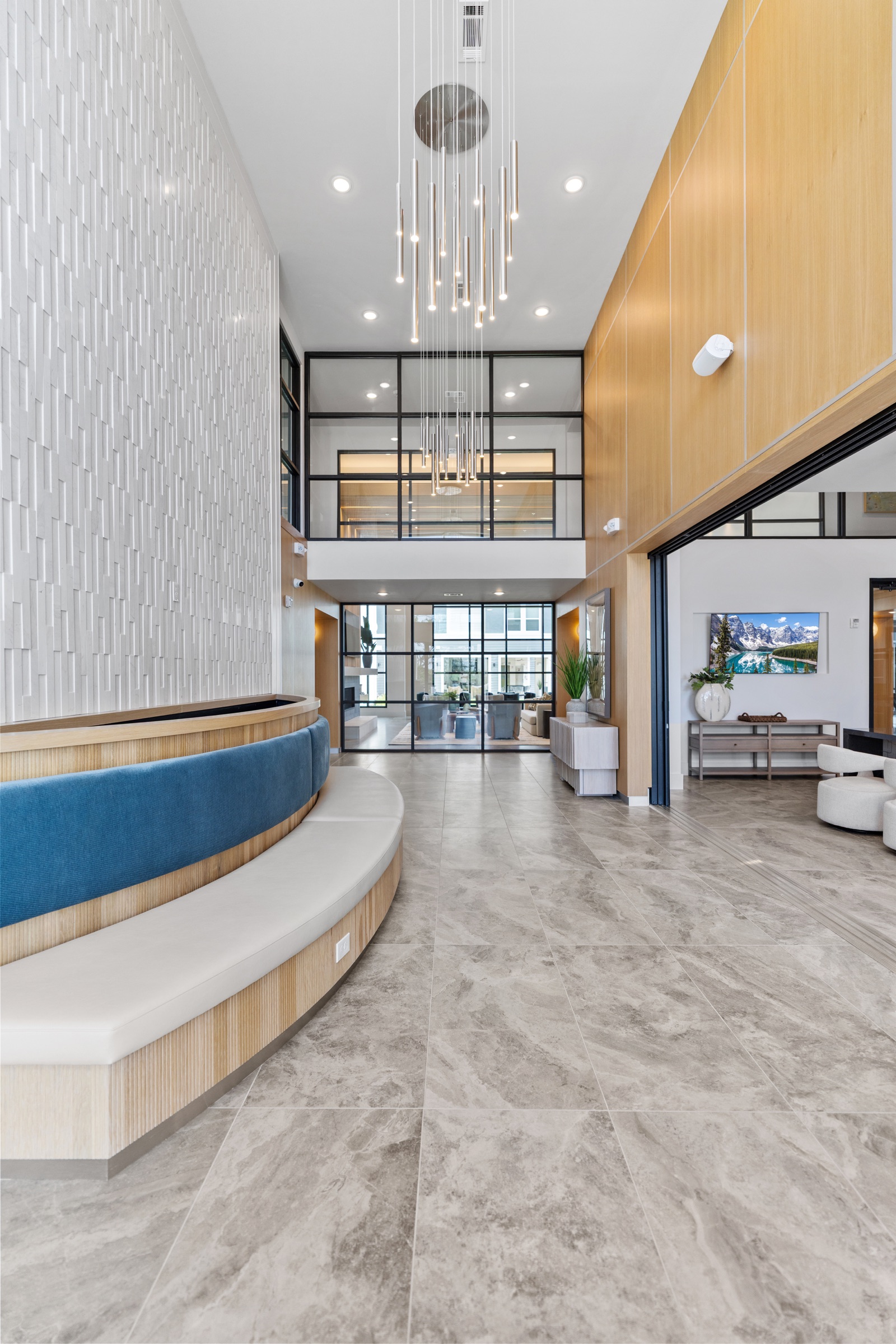 Double-height apartment lobby with a sculpted reception bench, wood paneling and pendant lights