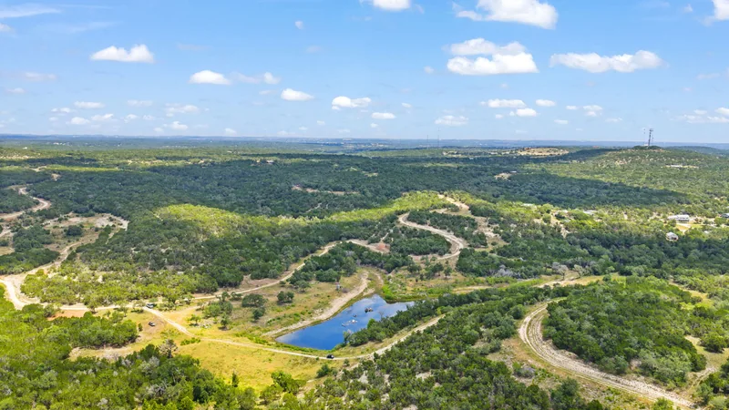 Aerial view across Hill Country ranchland with a pond and winding tracks