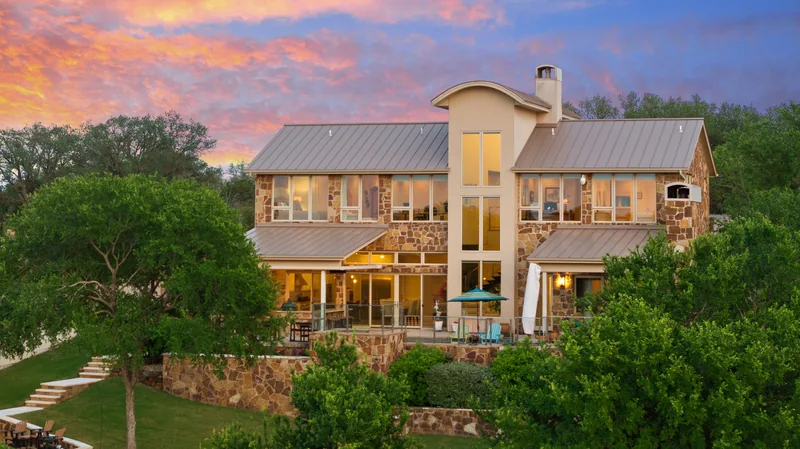 Stone home framed by trees beneath a pink and blue sunset