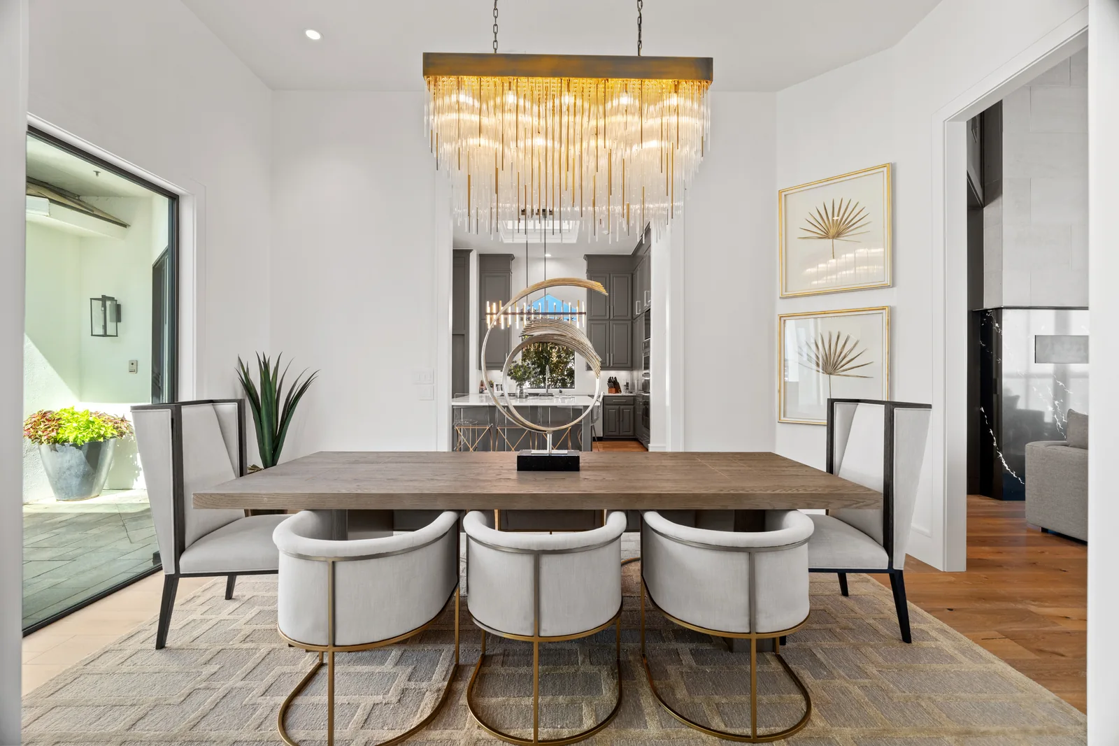 Dining table beneath a chandelier beside open living spaces
