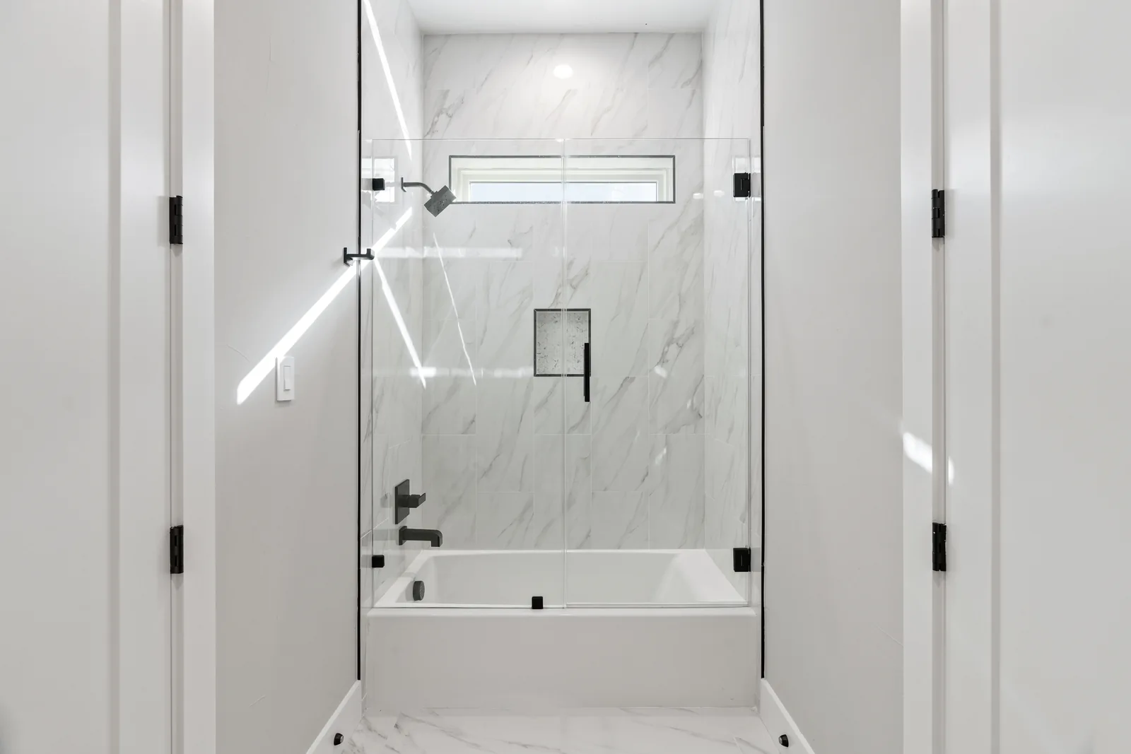 Glass-enclosed shower with marble tile and black fixtures
