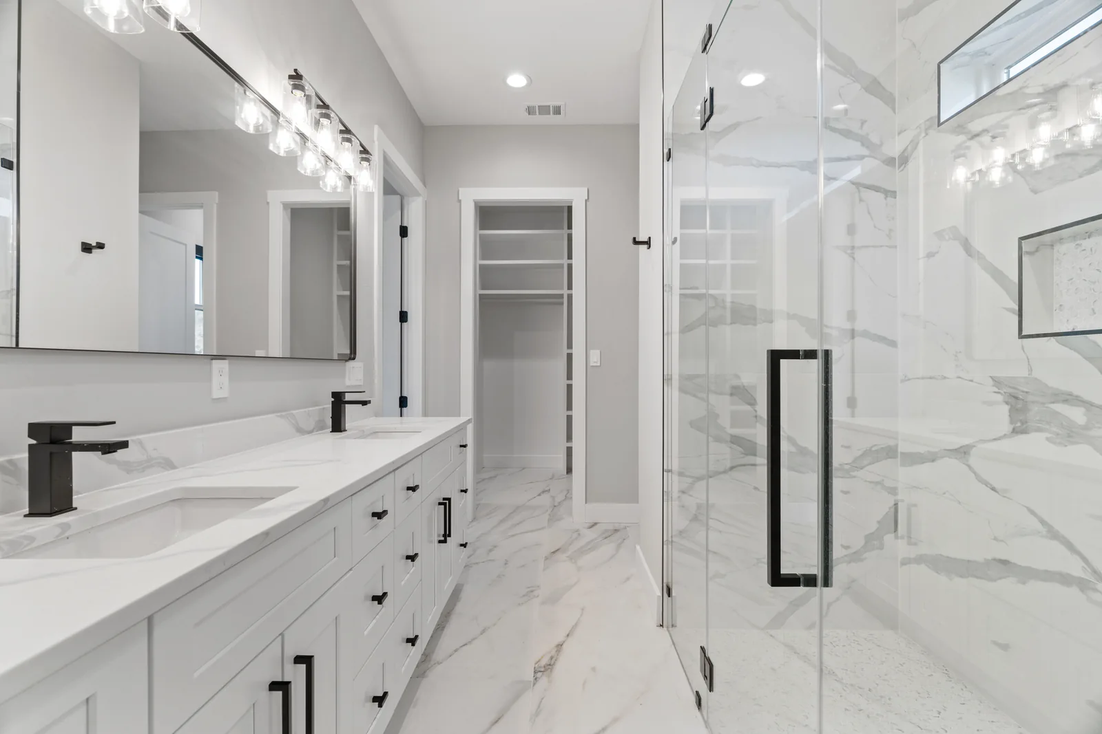 Light bathroom with double vanity, mirrors, and a glass shower