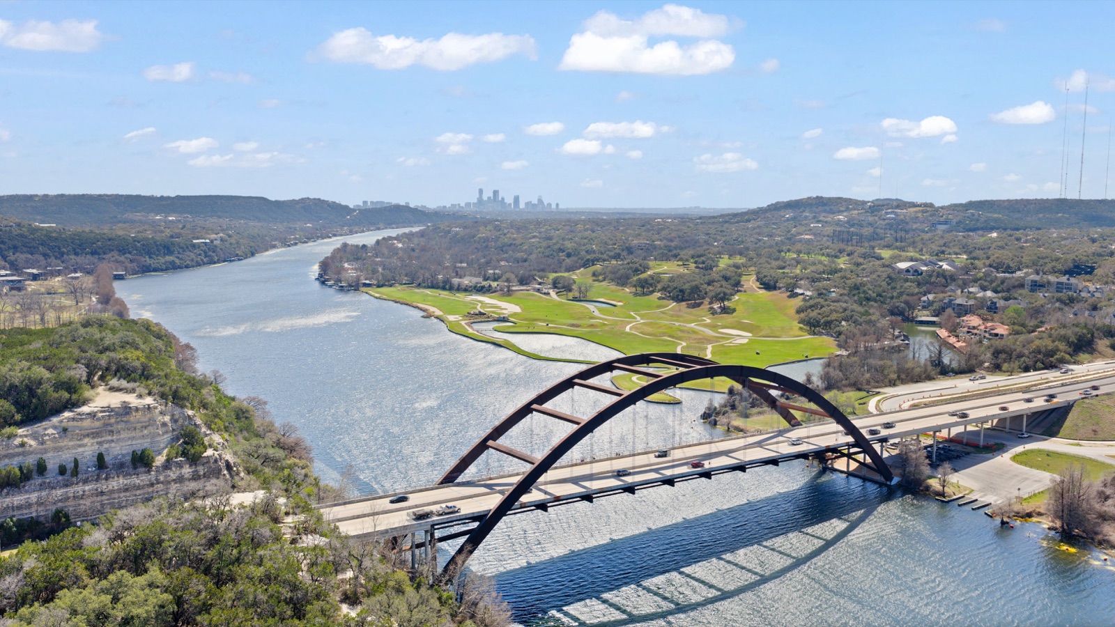 Aerial view of Pennybacker (Loop 360) Bridge crossing Lake Austin, with the Austin skyline in the distance