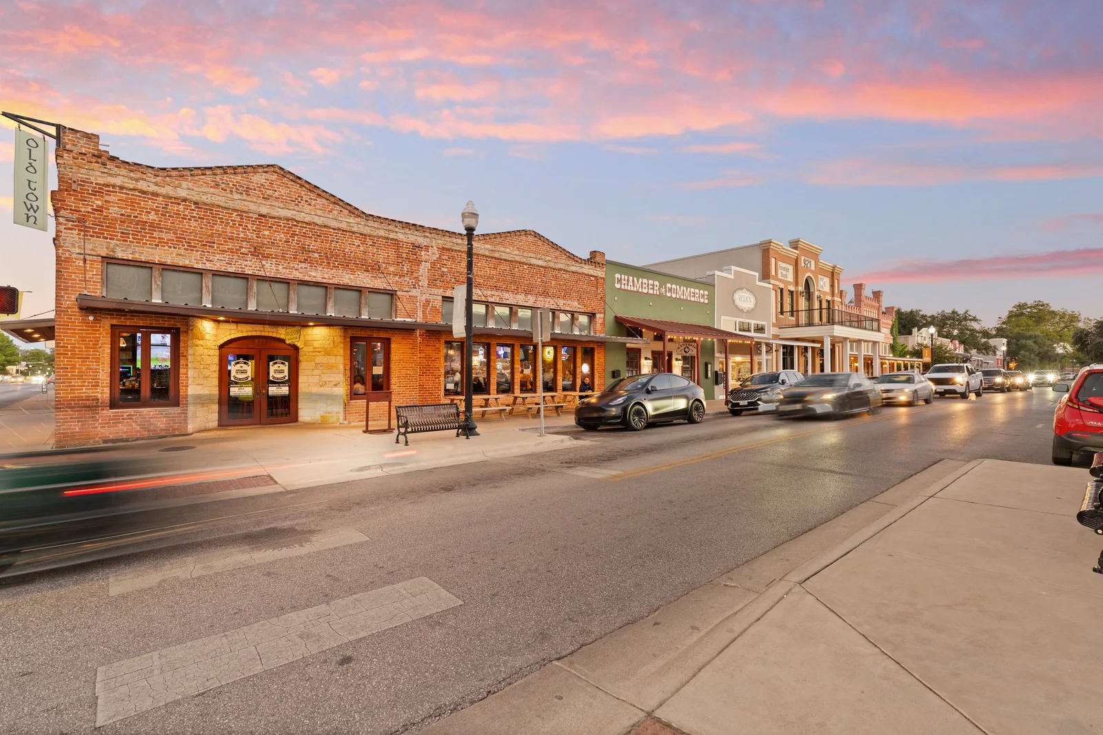 Brick storefronts and a streetscape under a pink evening sky