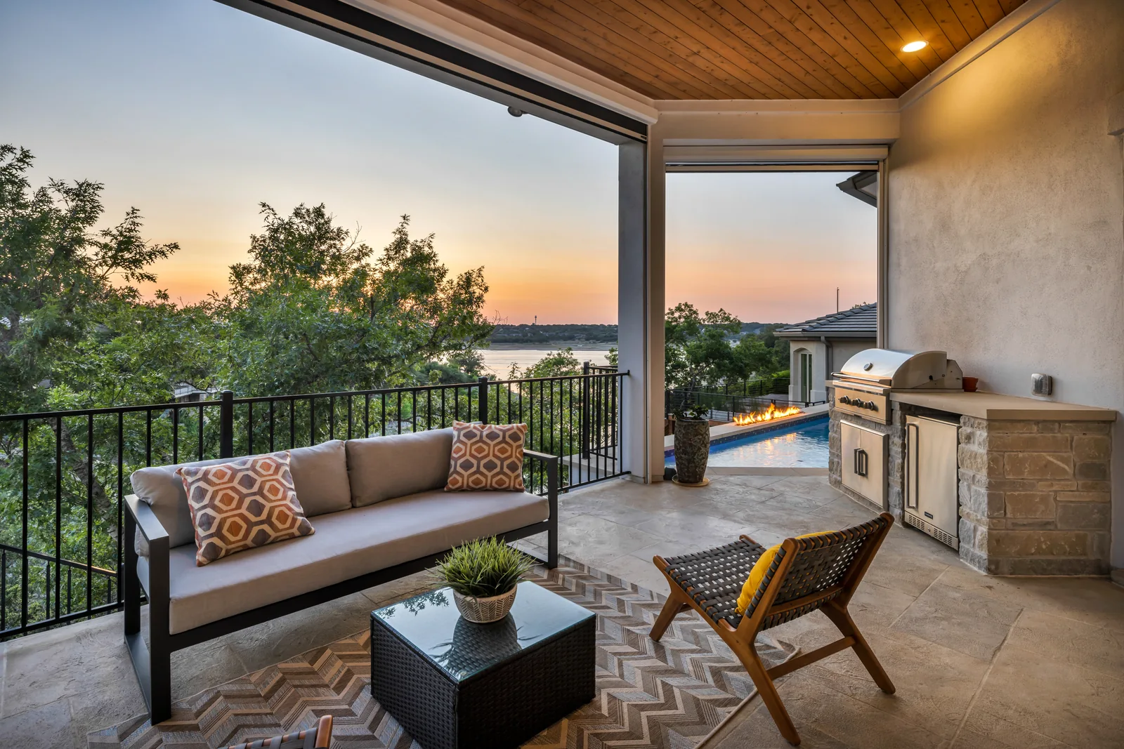 Covered patio with seating, an outdoor kitchen, and a lake view at sunset