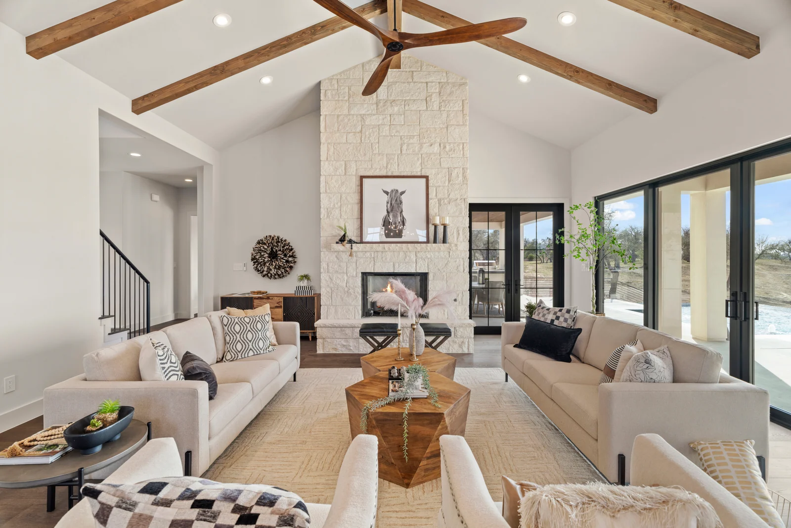 Light-filled living room with timber beams, a limestone fireplace, and generous windows