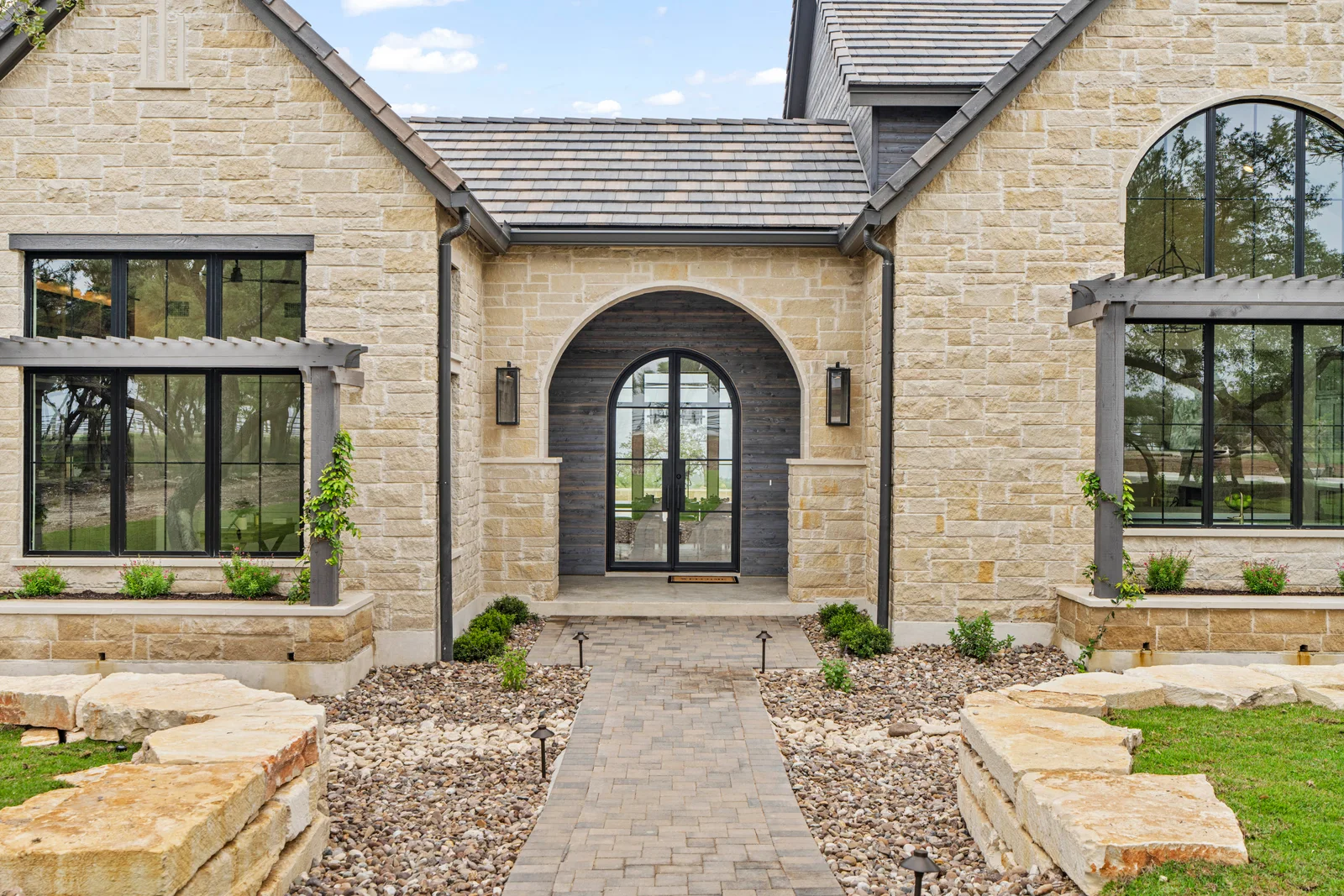 Limestone home facade with a recessed arched entry and dark framed windows