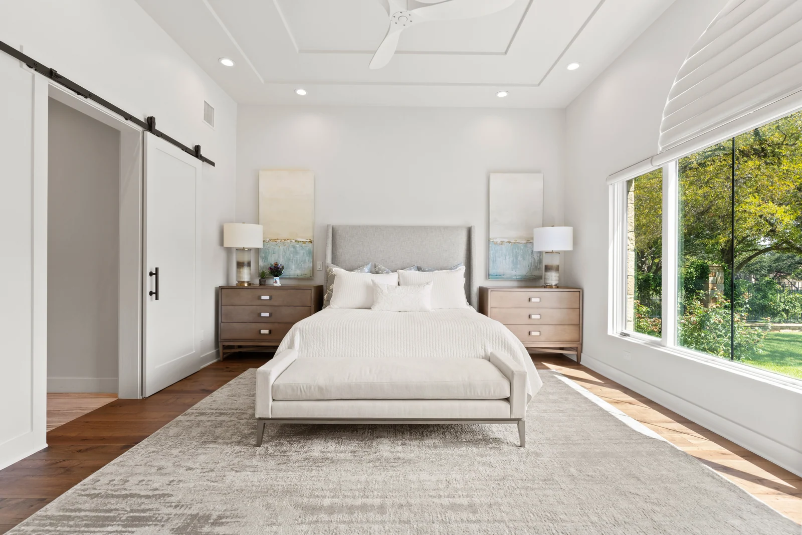 Serene bedroom with a white upholstered bed, warm wood nightstands, and sunlit garden views