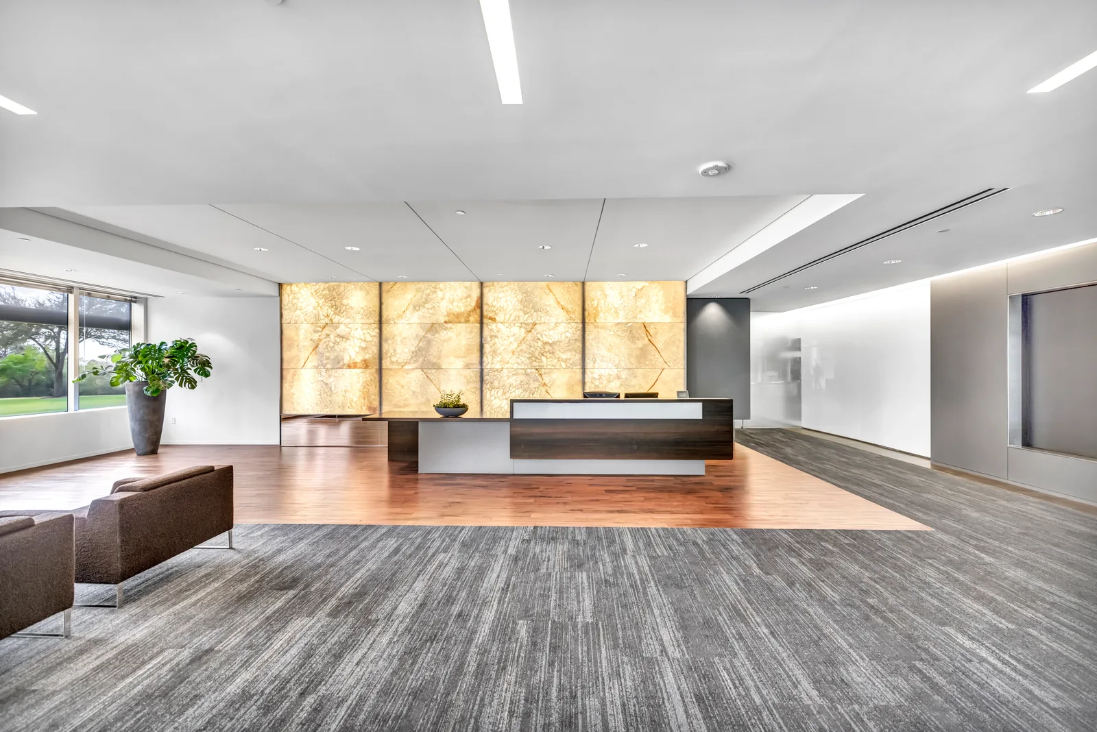 Commercial reception area with a backlit stone wall, wood desk and broad windows