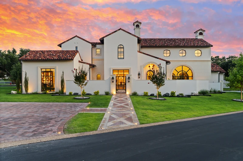 White home with a warmly illuminated entrance beneath a colorful sunset