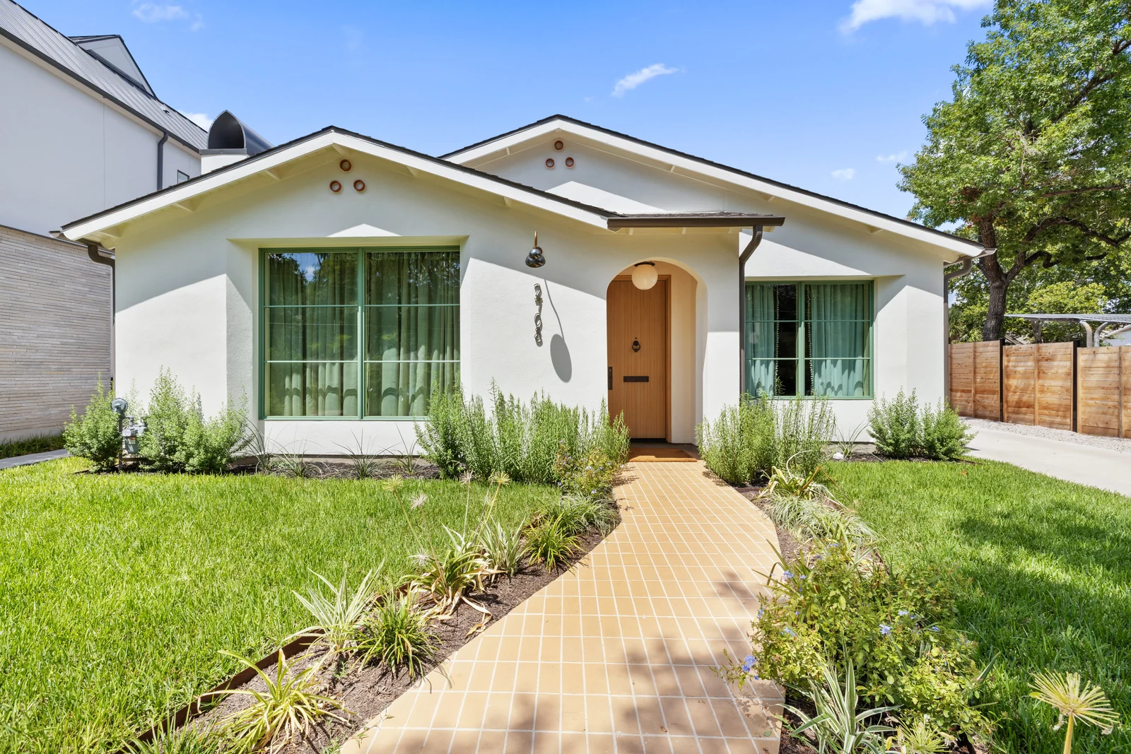 Sunlit white home with an arched wooden entry and a landscaped garden