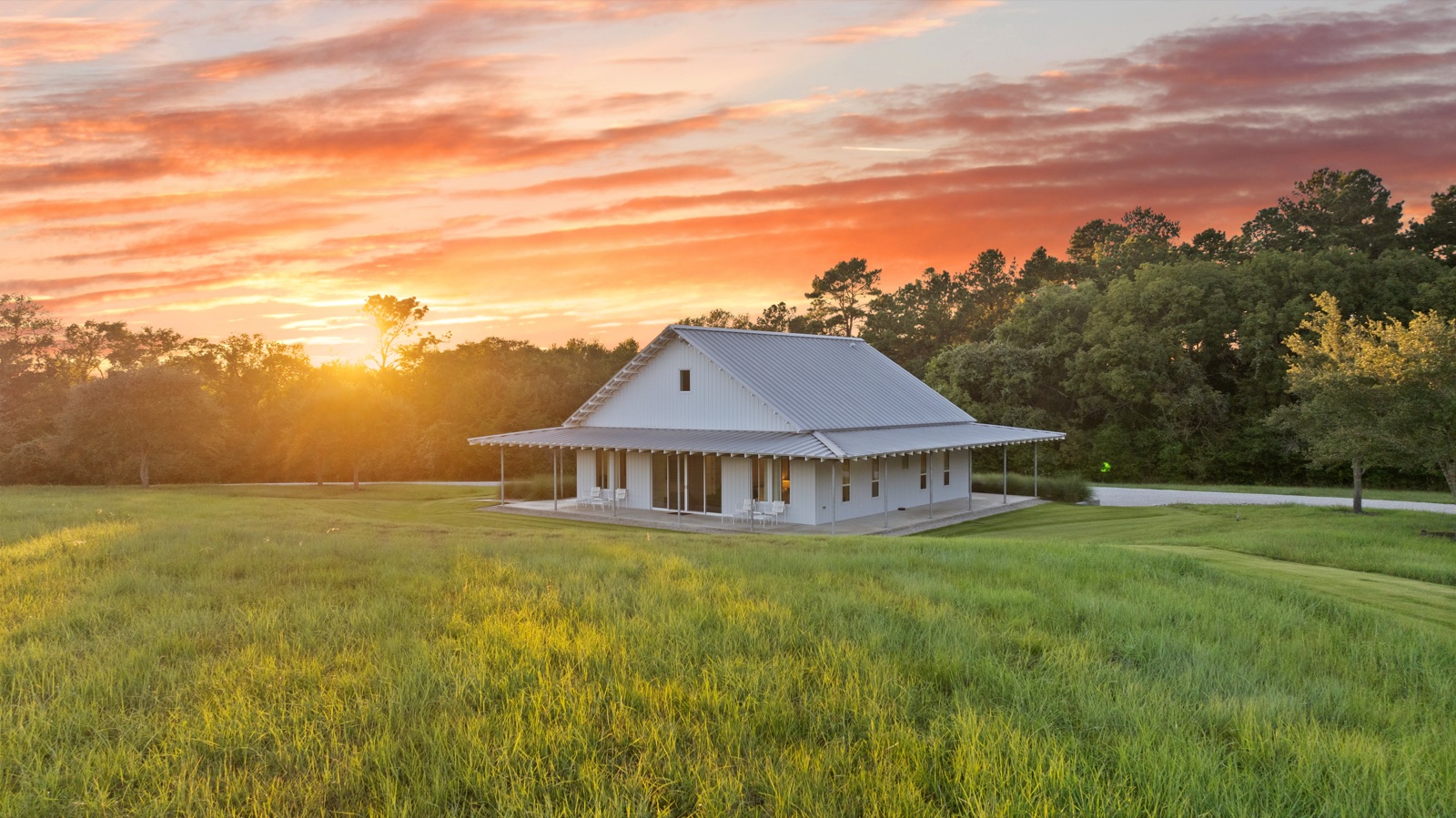 White ranch lodge in a field beneath a vivid orange sunset