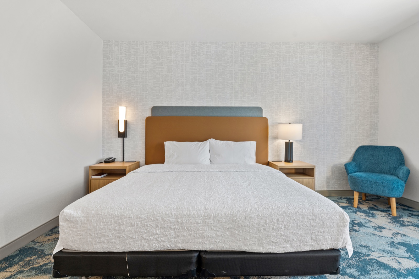 Hotel guest room with king bed and blue accent chair