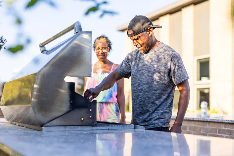 A man cooks at an outdoor grill while a woman looks on