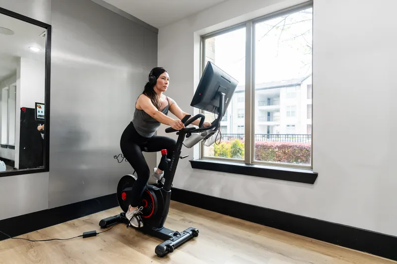 A woman cycles on an exercise bike beside a window in a fitness studio
