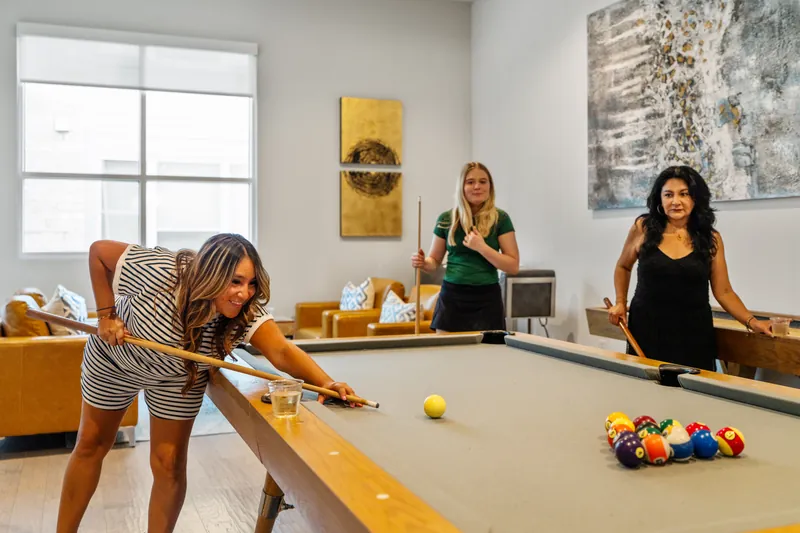 Three people play billiards in a shared lounge
