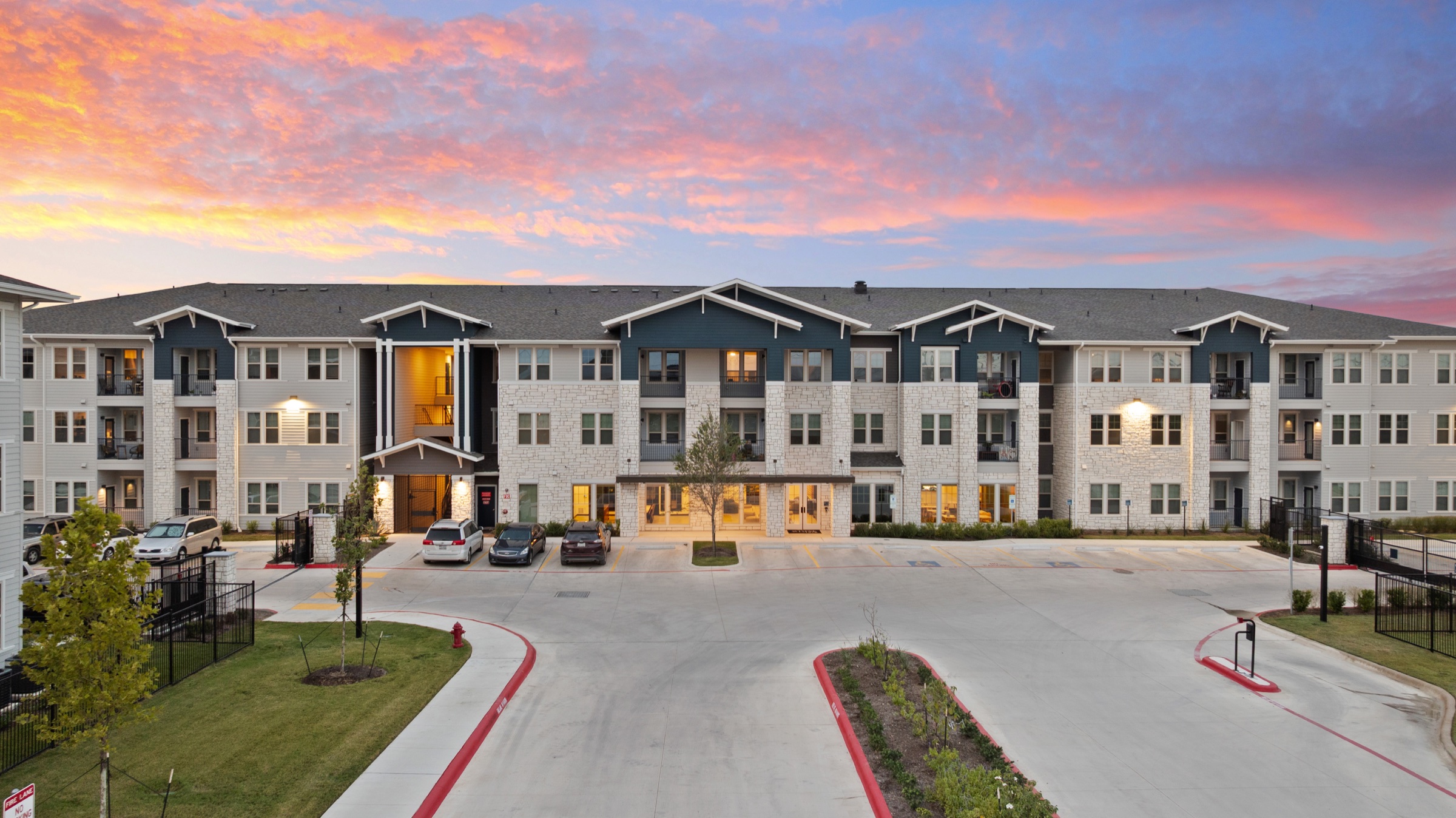 Apartment community exterior glowing beneath a pink and orange evening sky