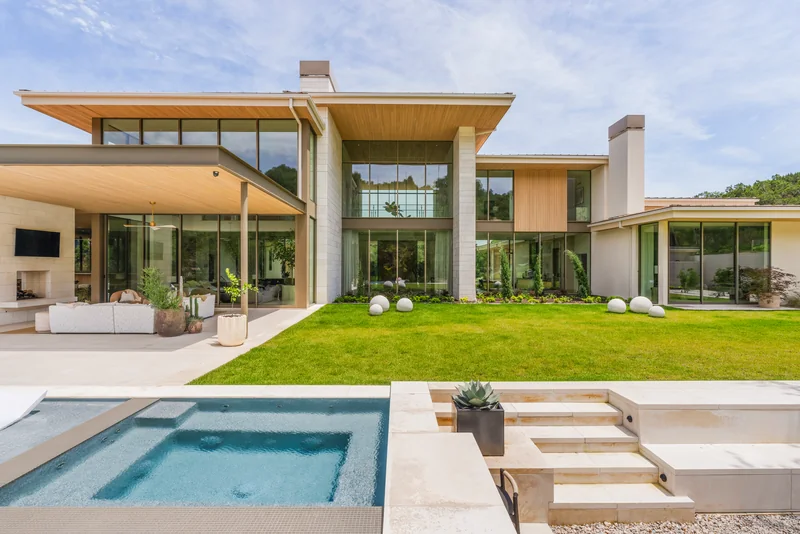 Contemporary stone and glass home with deep timber roof overhangs, landscaped lawn and a pool