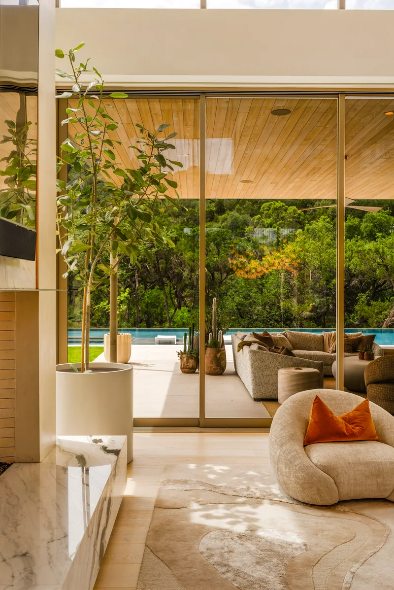 Sunlit lounge with curved seating, stone flooring and full-height glass doors opening to a garden