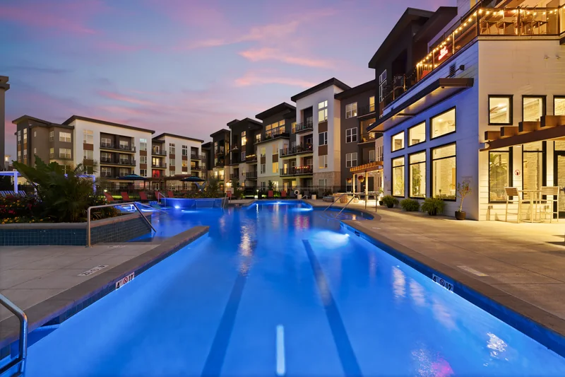 Apartment buildings and clubhouse illuminated around a blue swimming pool at twilight