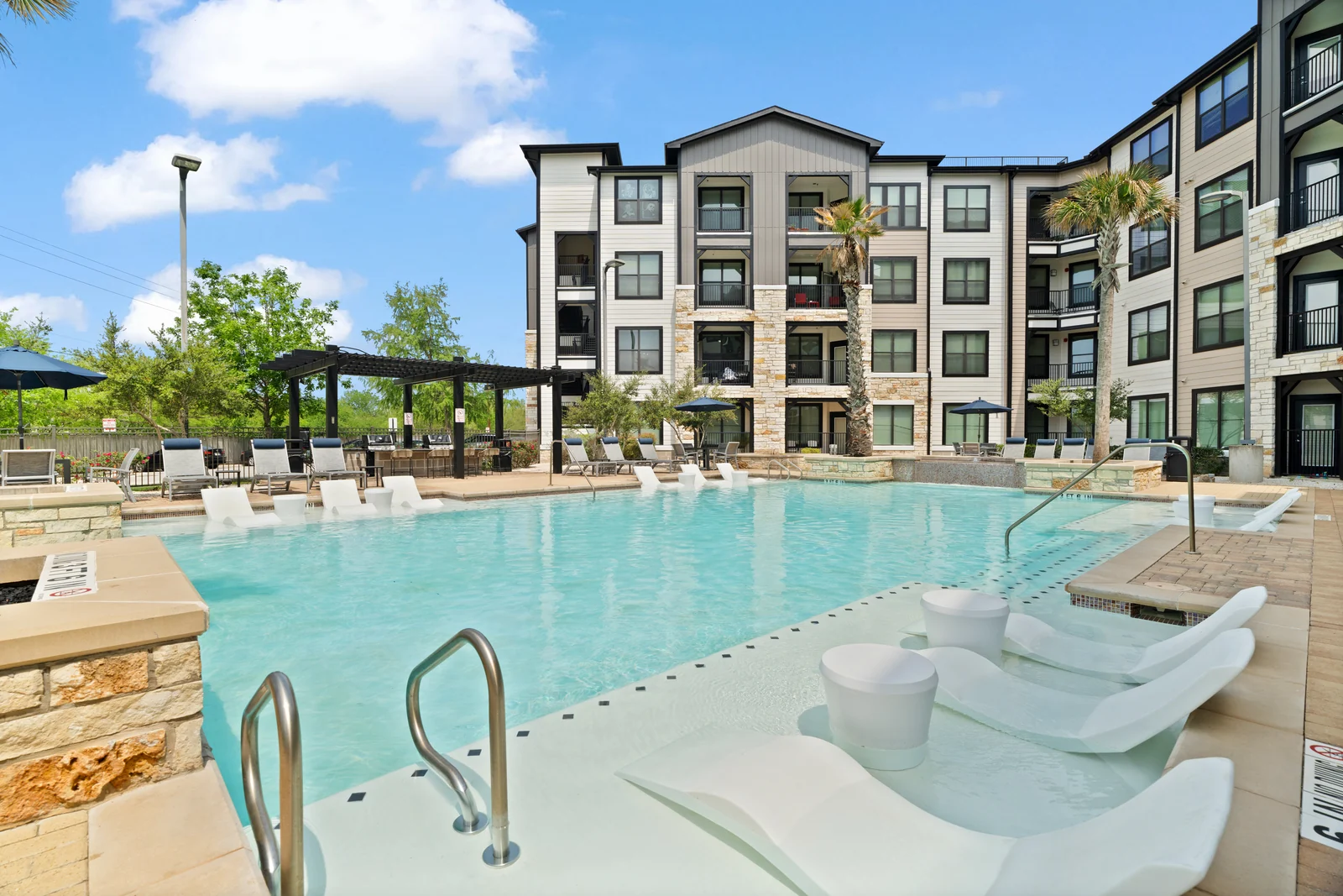 Apartment community swimming pool with in-water loungers and shaded outdoor seating.