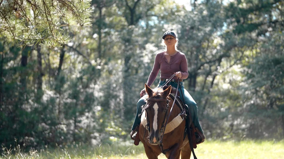 A rider on horseback moving through a wooded ranch